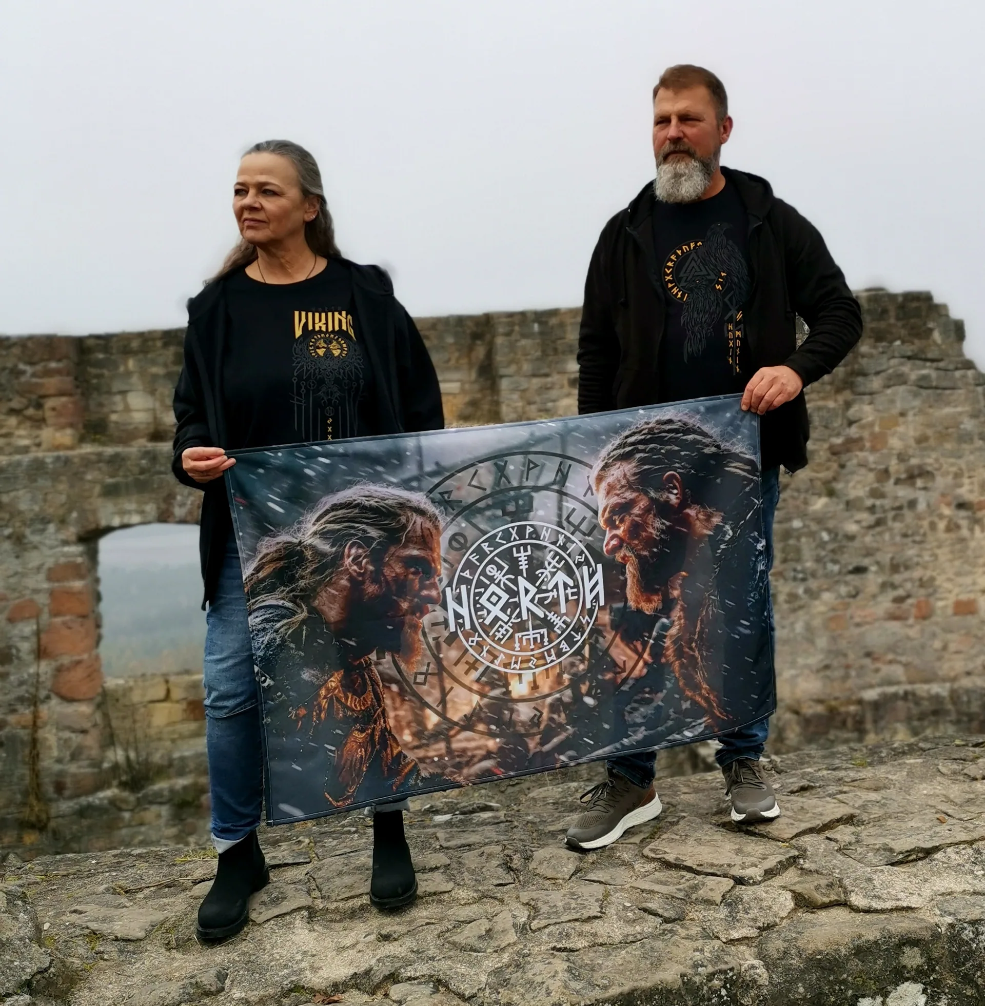 Paar präsentiert eine North Legendary Wikinger-Flagge auf der Mauer einer Burgruine im Nebel