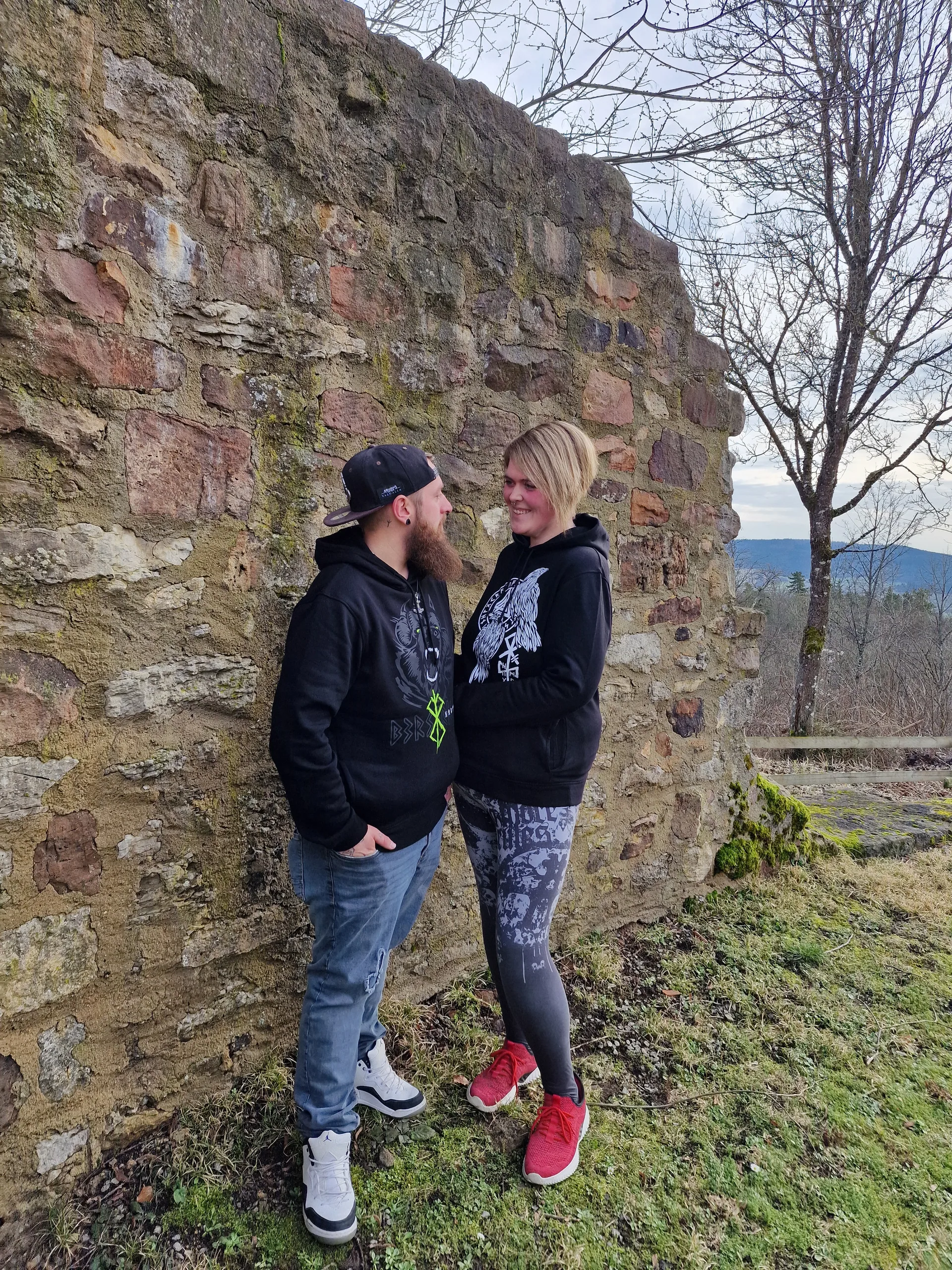 Paar in North Legendary Hoodies vor einer mittelalterlichen Burgruine, lachender Blickkontakt